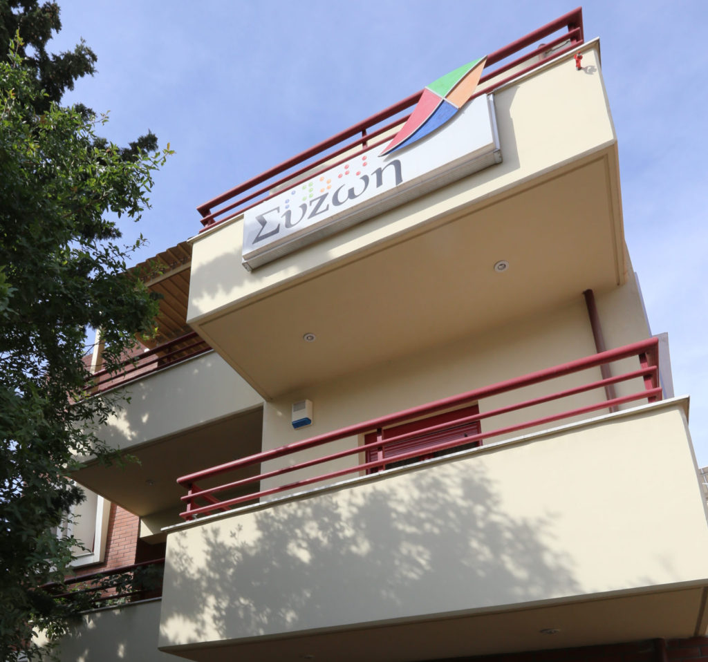 Φωτογραφία από το κτίριο της συζωής και την ταμπέλα με το λογότυπο της Συζωής στο μπαλκόνι του κτιρίου